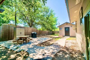 A backyard with a picnic table and barbecue grill, surrounded by a wooden fence and a small building. - Perfect Private Getaway in Buchanan Lake Village! (Tow)
