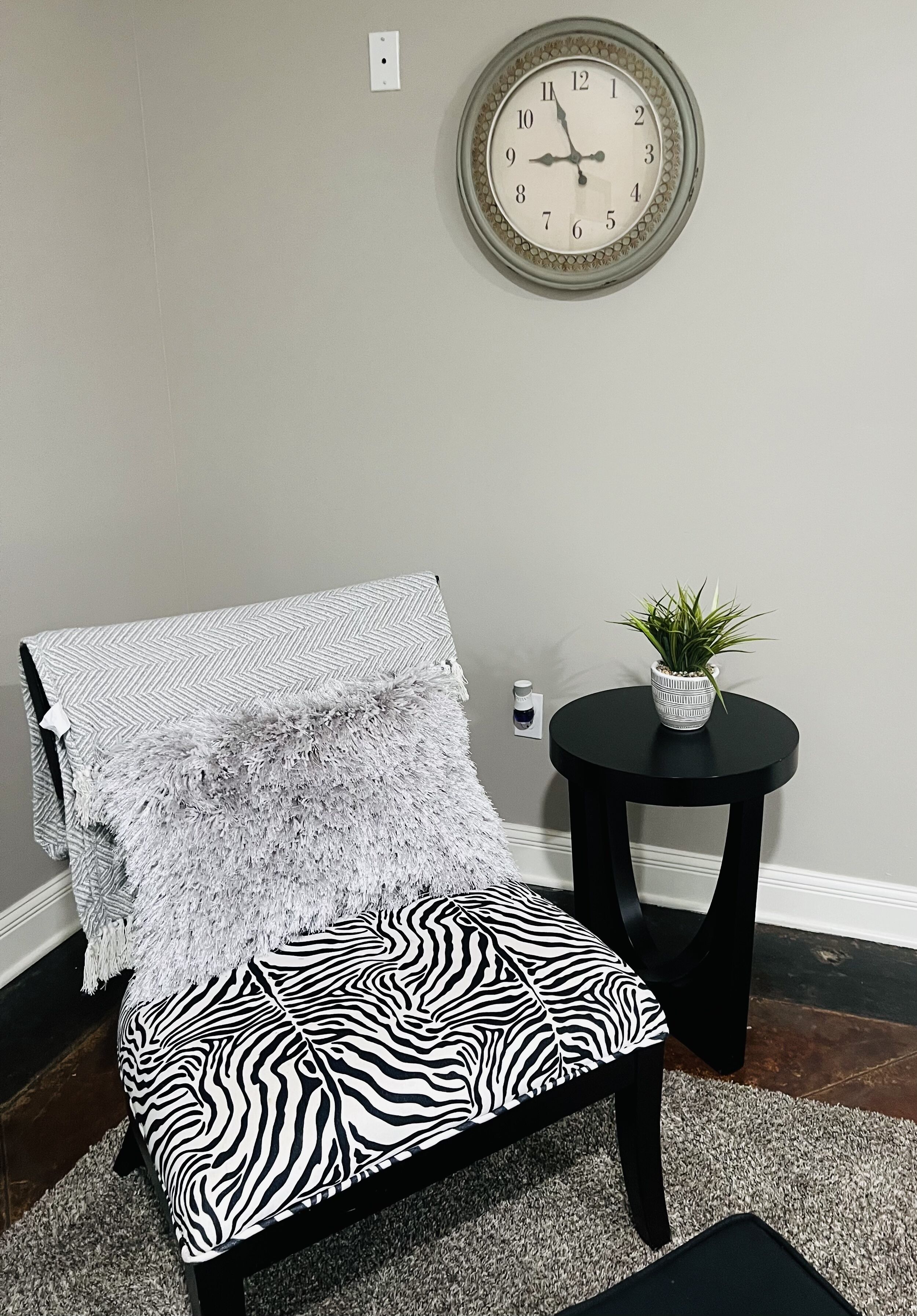 A chair with a zebra print cushion, a fluffy white throw, and a small potted plant on a black side table.