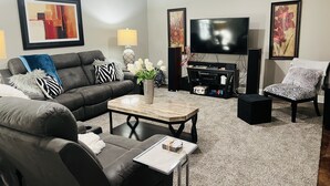 A modern living room with a grey sofa, a coffee table, a TV, and decorative pillows. - 10min from MIZZOU/Univ Hospital/downtown! Family sized, CLEAN! Short term avail! (Columbia)