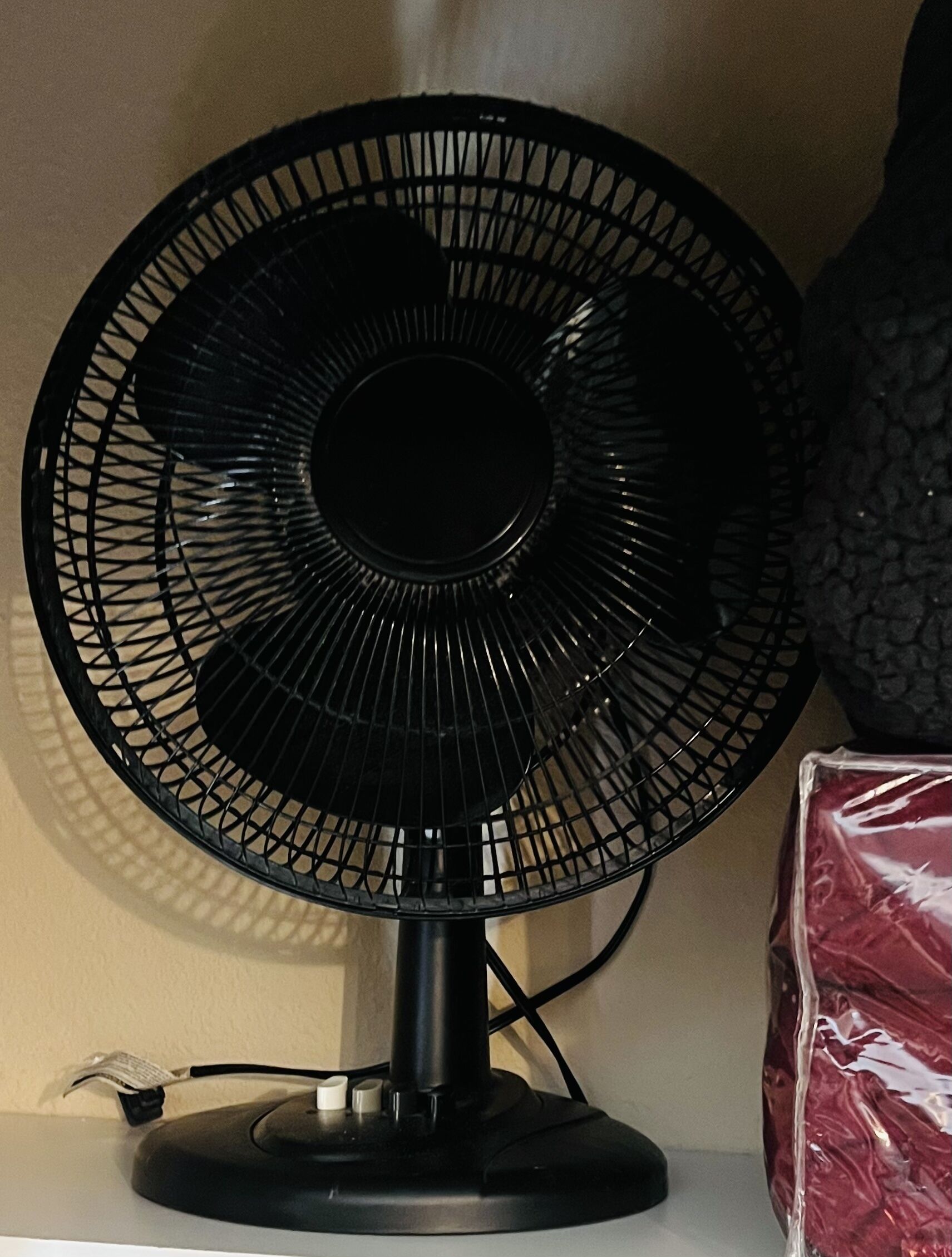 Ein schwarzer Standventilator mit kreisförmigem Grillgitter, platziert auf einer Oberfläche, verbunden mit einem Kabel.