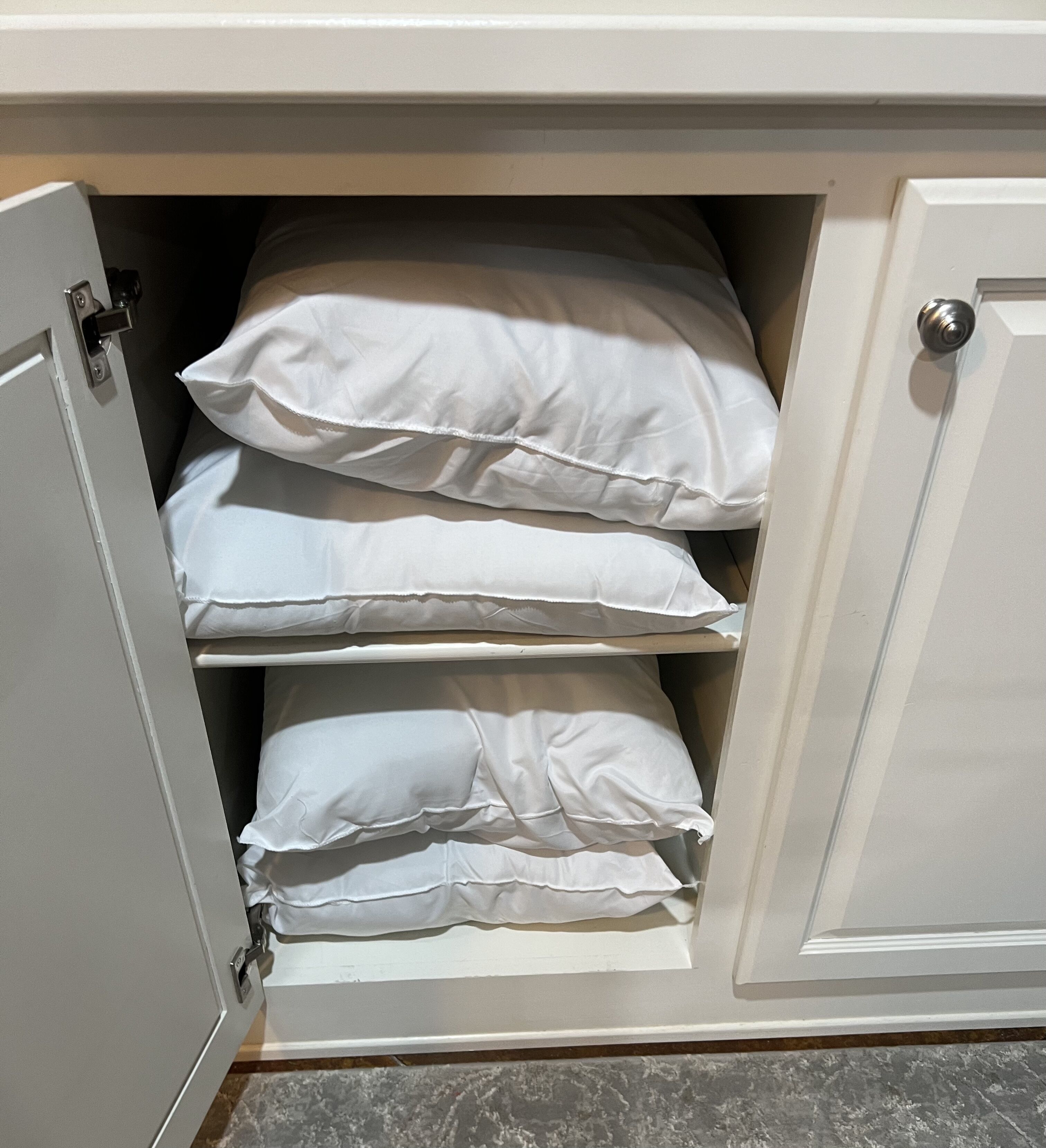 A storage cabinet with multiple shelves containing white pillows.