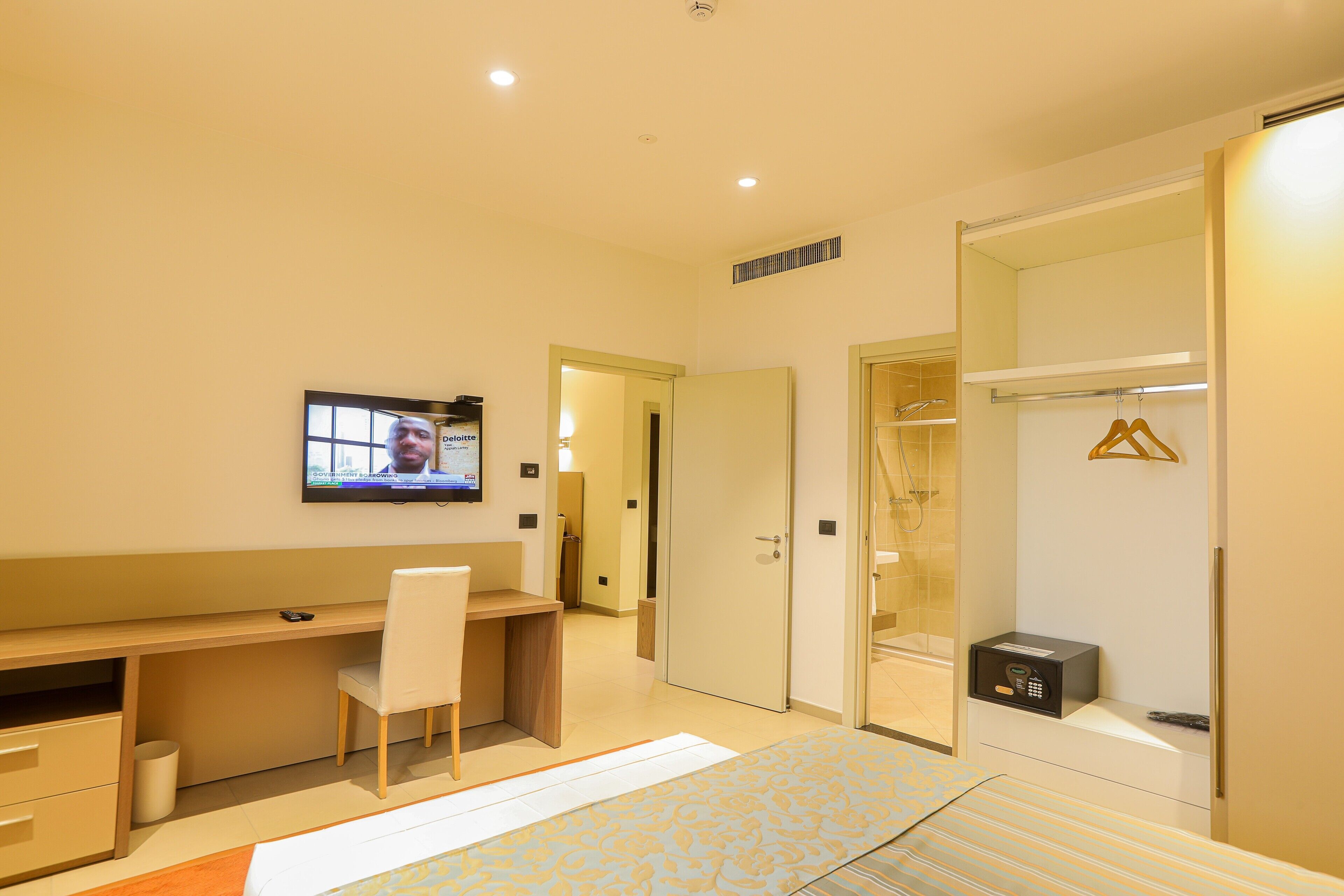 Une chambre d’hôtel équipée d’un bureau, d’une chaise, d’un lit, d’une télévision, d’une armoire et d’un petit coffre-fort.