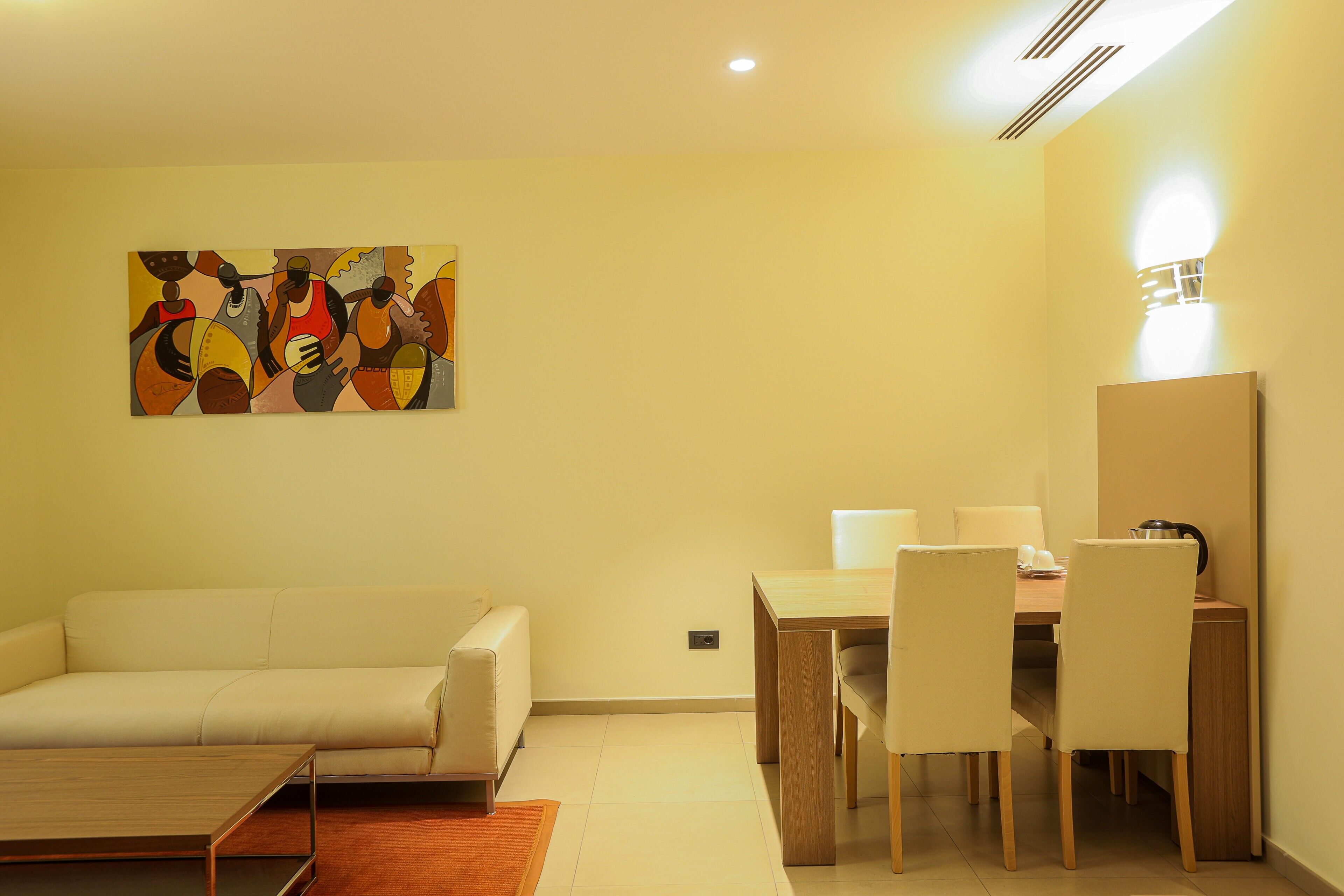 Una sala de estar moderna con un sofá, una mesa de comedor con sillas, una mesa de centro y una obra de arte colgada en la pared.