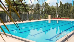 A clear blue swimming pool with lane markers, surrounded by a green fence and potted plants.