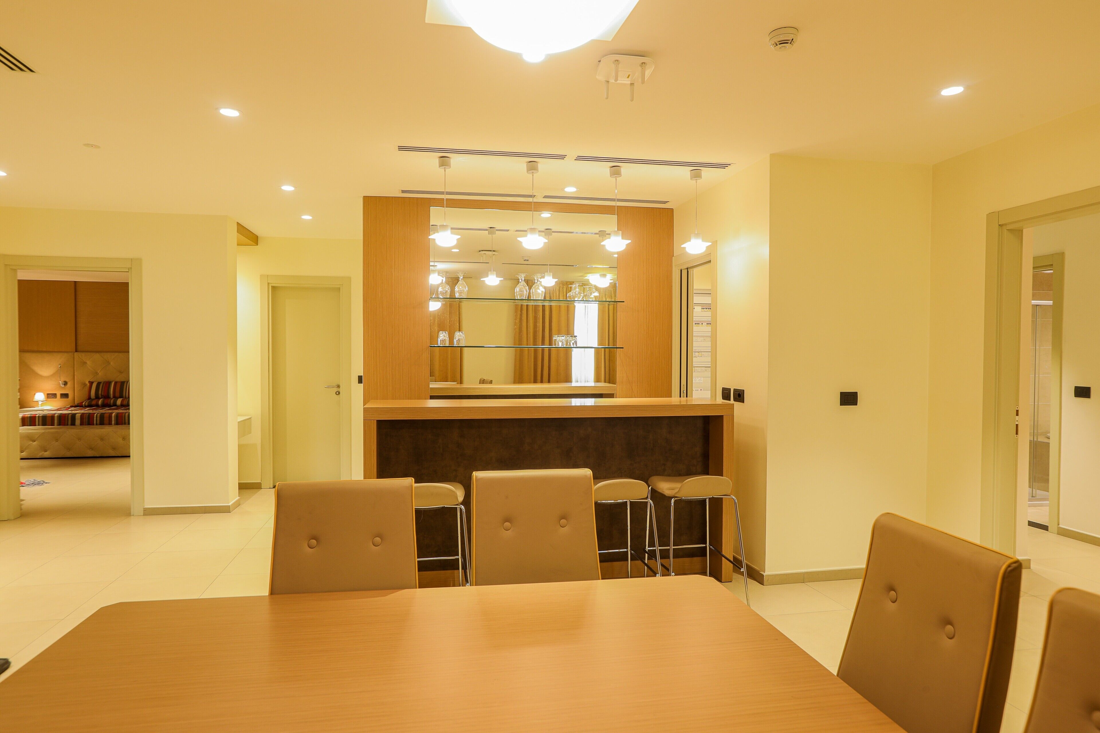A modern dining area with a wooden table and chairs, a glass partition, and a mirror above the counter.