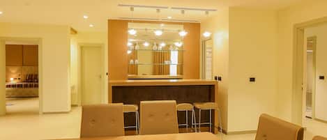 A modern dining area with a wooden table and chairs, a glass partition, and a mirror above the counter.