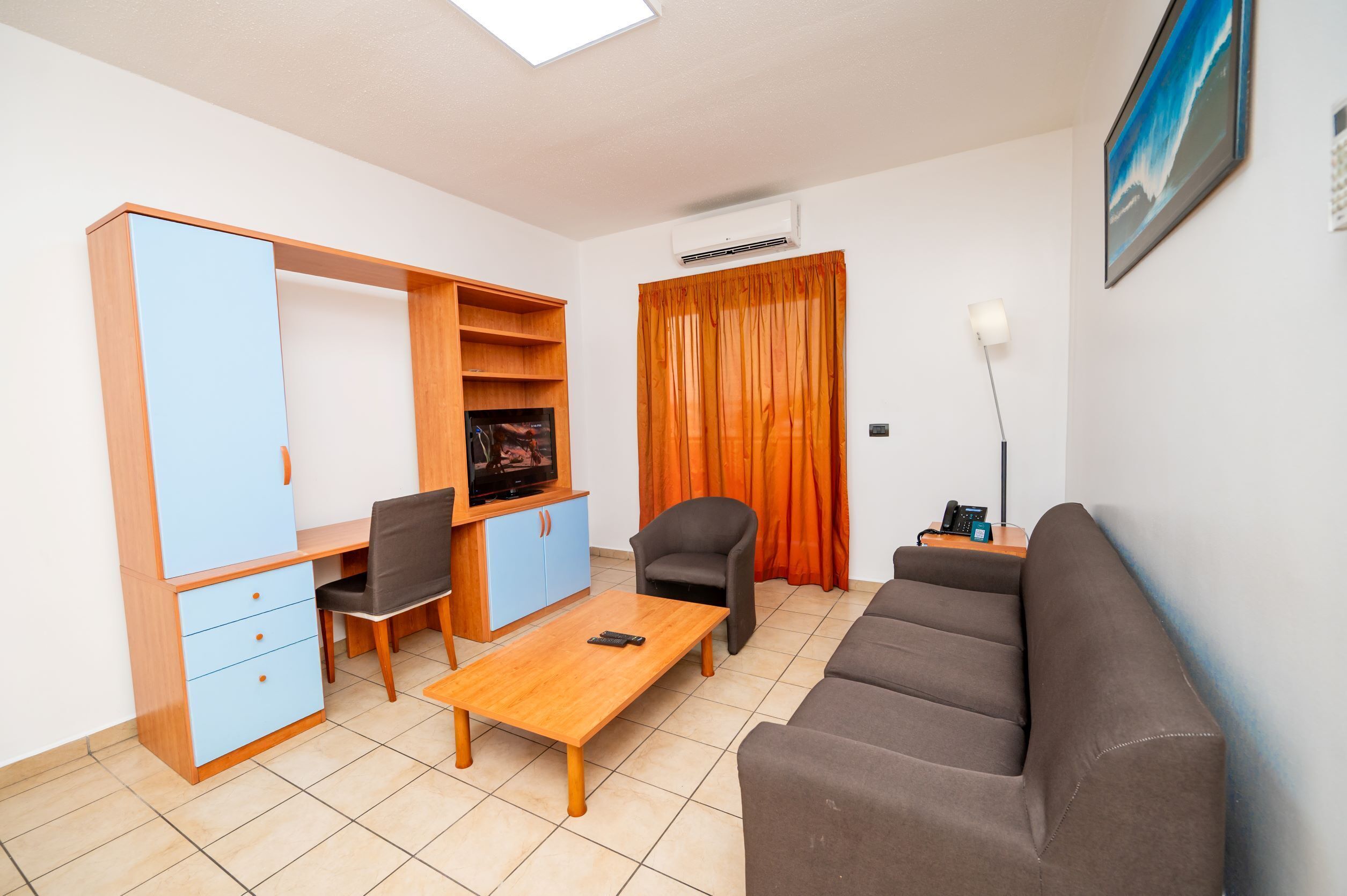 En kompakt opholdsstue med sofa, skrivebord med stol, TV og garderobeskab.