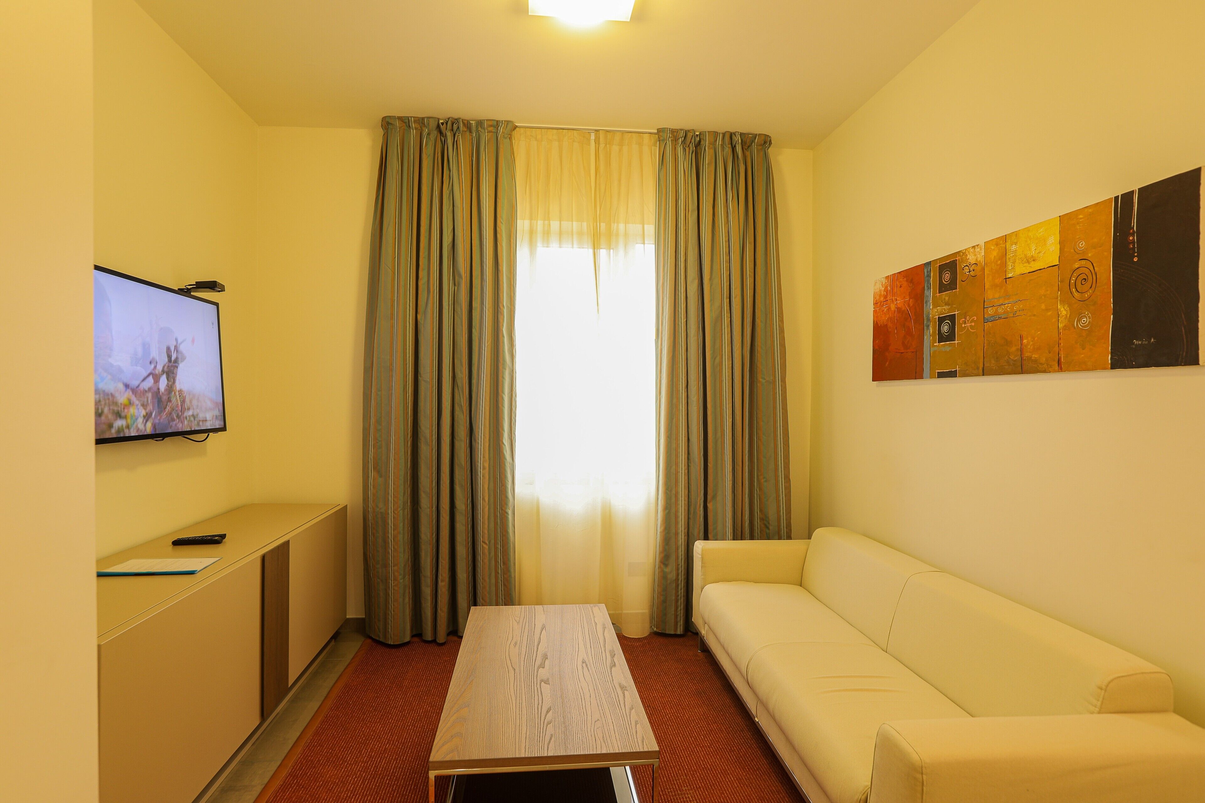Una habitación de hotel con televisión, sofá, mesa y ventana con cortinas.