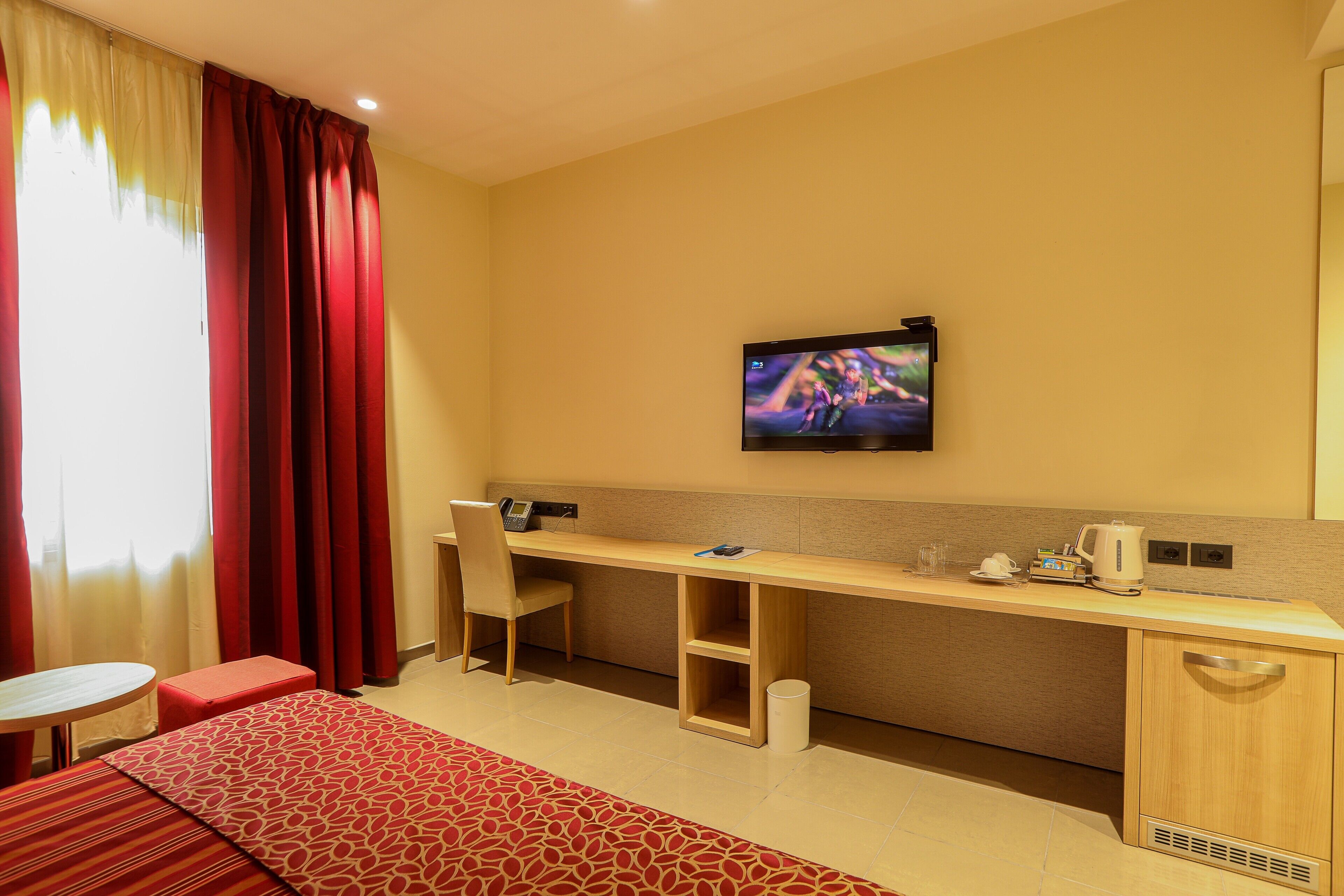 A hotel room with a desk, chair, and a television mounted on the wall.