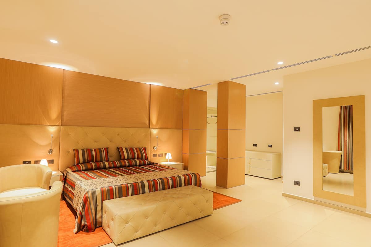 Une chambre d’hôtel moderne avec un grand lit, un coin salon comprenant un fauteuil, une petite table et un miroir.