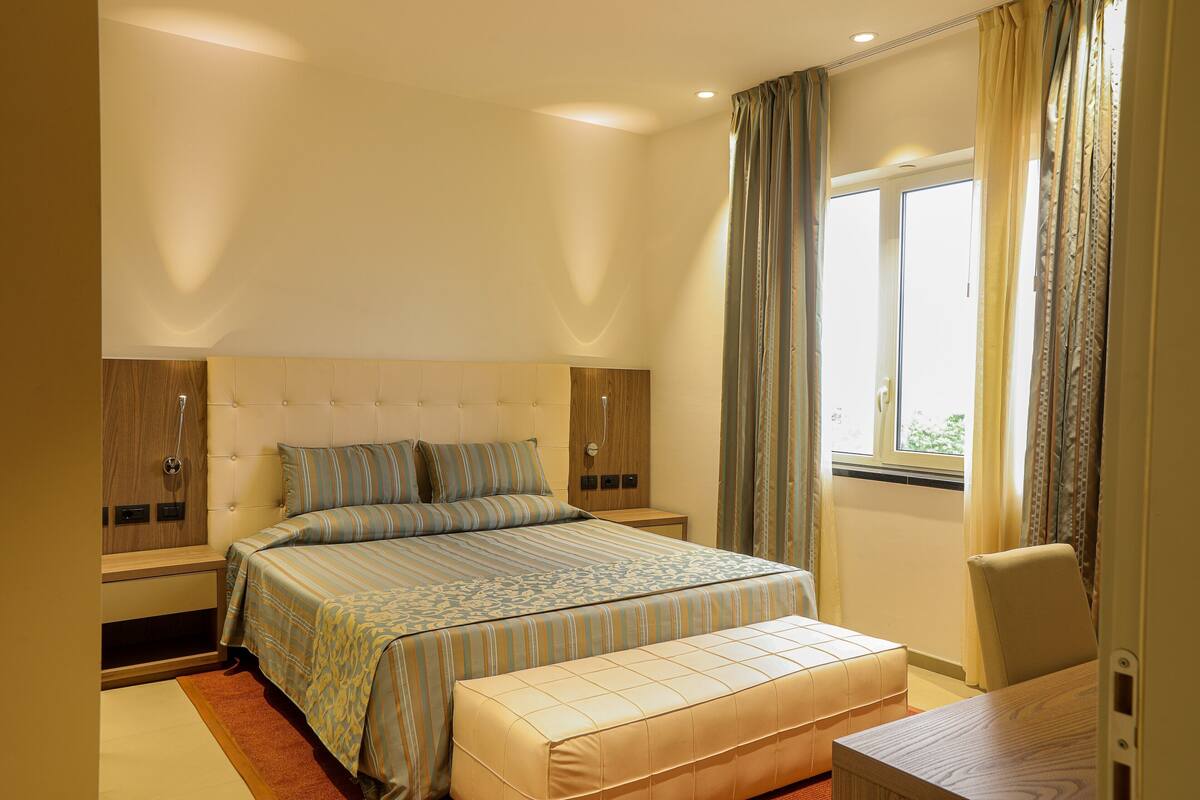 Une chambre à coucher avec un lit, des tables de chevet, une chaise et une fenêtre avec des rideaux.