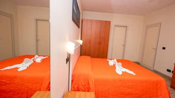 Habitación de hotel con dos camas, un armario de madera, una lámpara fijada a la pared y suelo de baldosas.