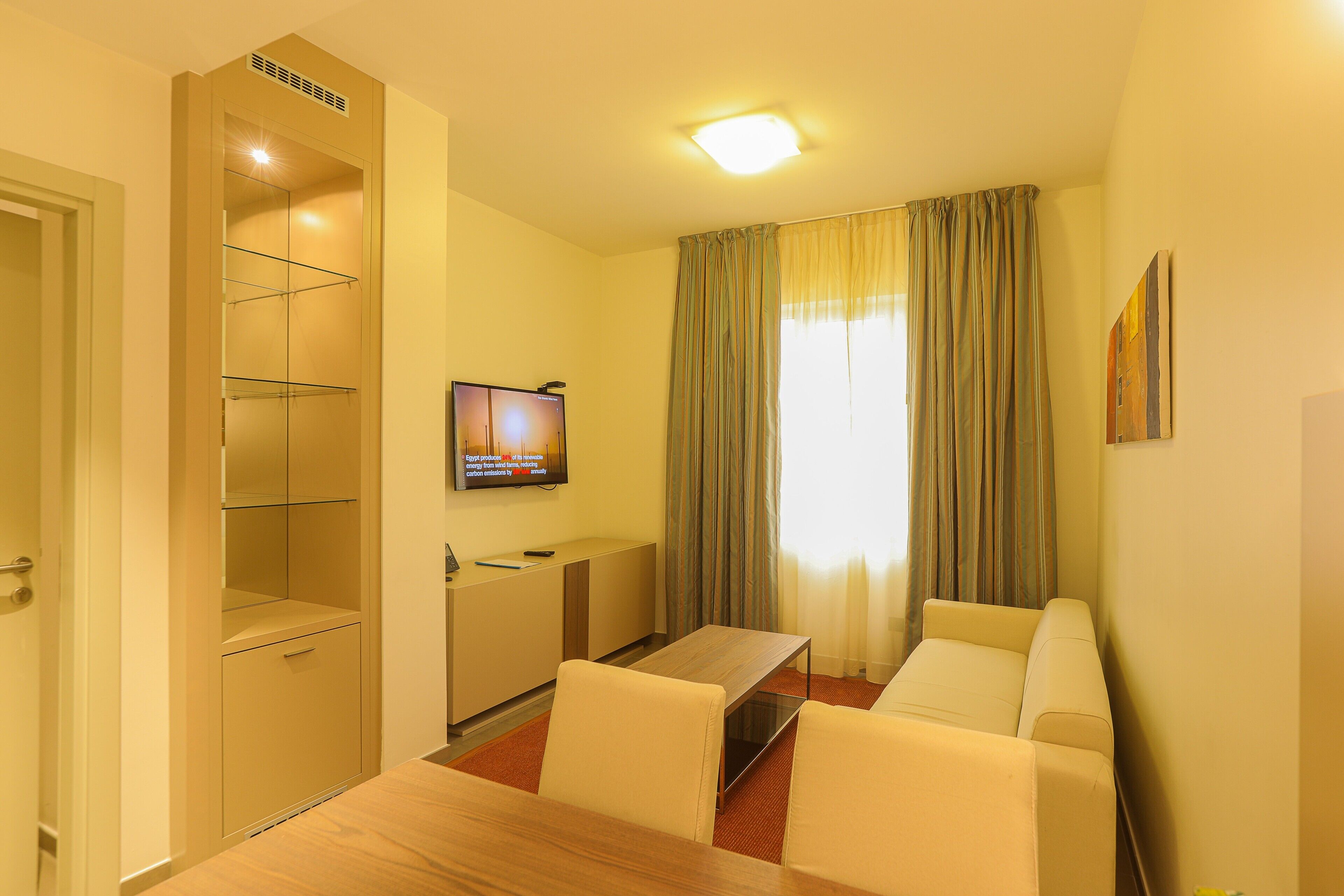Une chambre d’hôtel avec une table à manger en bois, deux chaises, un téléviseur fixé au mur, un bureau et une armoire.