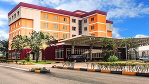 A multi-story hotel with a red and orange facade, a covered entrance, and palm trees in the foreground.