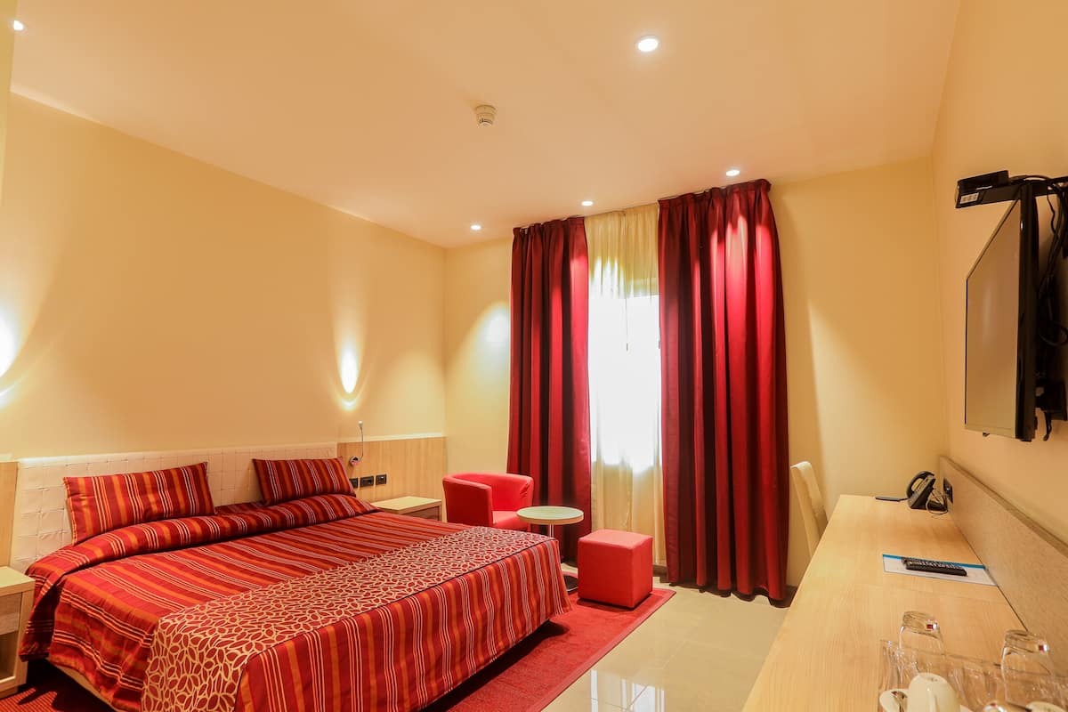 Une chambre d’hôtel avec un grand lit, un bureau, une chaise, une petite table et un téléviseur.