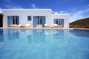Ein Poolbereich mit drei Liegestühlen, einem klaren Pool und einem weißen Gebäude mit blauen Fensterläden.