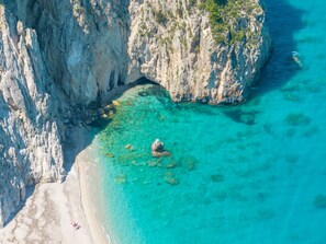 A coastal cliff with a clear turquoise sea and a sandy beach. - Villa Panorea, a hidden gem with unobstructed views (Άγιος Νικήτας)