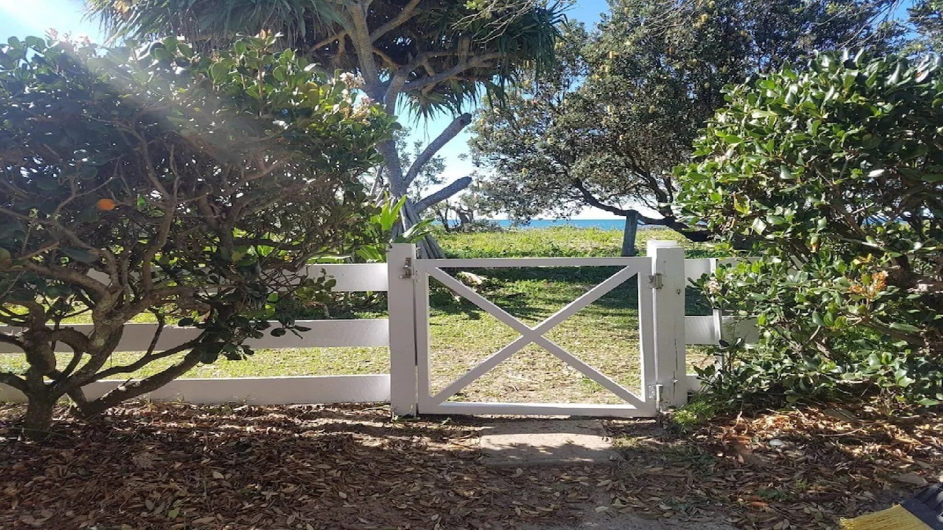 A gated entrance with a white gate, surrounded by trees and a grassy area.