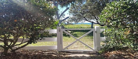 A gated entrance with a white gate, surrounded by trees and a grassy area.