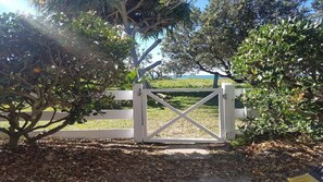 A gated entrance with a white gate, surrounded by trees and a grassy area.