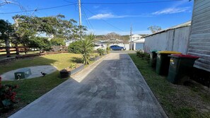 A residential driveway with a car parked on the side, a small garden area with plants, and a utility box.