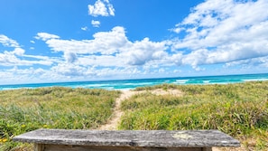 A wooden bench overlooking a beach with a clear sky and ocean view.