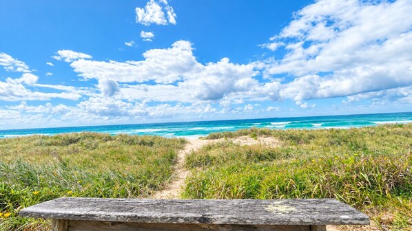 A wooden bench overlooking a beach with a clear sky and ocean view.