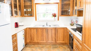A kitchen with wooden cabinets, a white countertop, a sink, a toaster, and a window with a flower vase.
