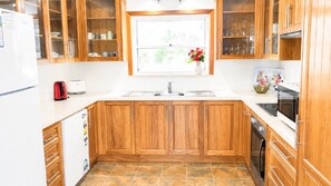 A kitchen with wooden cabinets, a white countertop, a sink, a toaster, and a window with a flower vase.