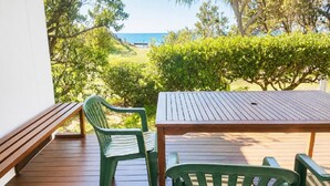 Een houten terras met een tafel en twee stoelen, met uitzicht op een strand en begroeiing.