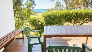 Een houten terras met een tafel en twee stoelen, met uitzicht op een strand en begroeiing.