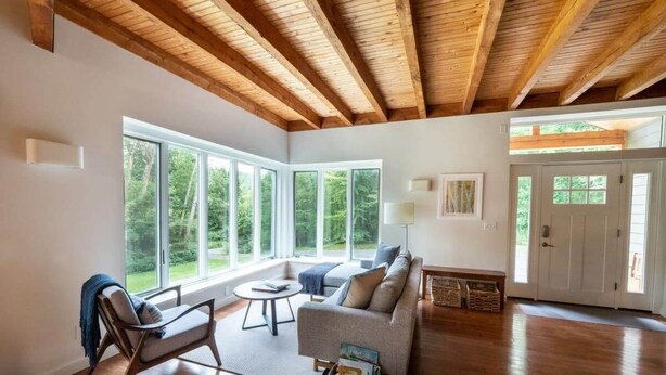 A spacious living room with hardwood floors, a wooden ceiling, and large windows offering a view of greenery. - Catamount, Zip Line, Private Setting, Book Now! (Egremont)