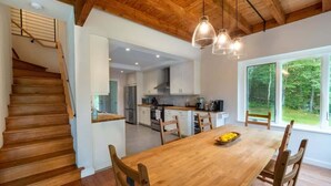 A modern kitchen with white cabinets, a wooden staircase, and a dining area with a wooden table and chairs. - Catamount, Zip Line, Private Setting, Book Now! (Egremont)