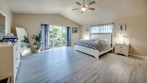 Um quarto espaçoso com uma cama grande, um ventilador de teto, uma mesa de cabeceira e vista para o exterior.