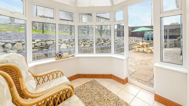 A conservatory with a stone wall, wicker furniture, and a view of the garden. - 3 bedroom accommodation in Cerrigydrudion (Cerrigydrudion)