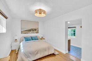 A bedroom with a bed, a nightstand, a lamp, a picture on the wall, and a window.
