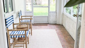 A covered patio with a white ceiling, a wooden table with striped cushions, and a view of a backyard through glass doors. - Boho Beach Villa- minutes to the ocean  (Vero Beach)