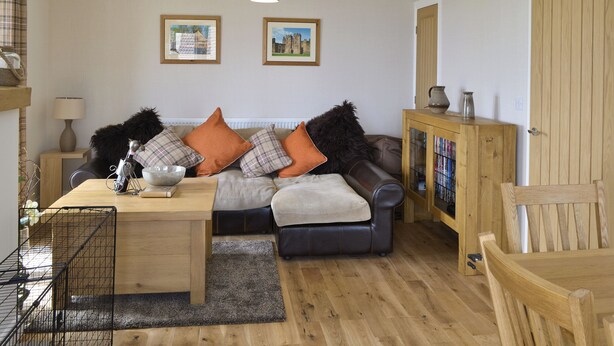 A cozy living room with a sofa, a wooden cabinet, and a dining table. - Belford House @ Seahouses (Seahouses)