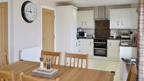 A modern kitchen with white cabinets, a microwave, oven, and a clock on the wall. - Belford House @ Seahouses (Seahouses)