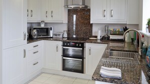 A kitchen with white cabinets, a microwave, a stove, and a sink with a dish rack. - Belford House @ Seahouses (Seahouses)