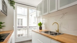 Une cuisine moderne avec des armoires blanches, un pare-feu en marbre, un plan de travail en bois et un évier en acier inoxydable doté d’un robinet doré.