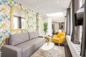 A modern living room with a grey sofa, a yellow armchair, a white coffee table, and a large mirror. - Merveil - Family suite - Louvre - Victoires (Paris)