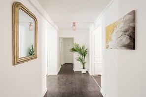 A hallway with a large mirror, a potted plant, and a painting on the wall. - Merveil - Family suite - Louvre - Victoires (Paris)
