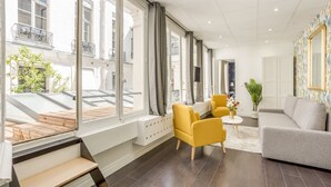 Un salon moderne avec un canapé gris, des fauteuils jaunes et un escalier en bois menant à un espace extérieur.