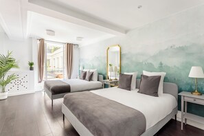 Une chambre d’hôtel moderne avec deux lits, un grand miroir, une table de chevet avec une lampe et une vue sur l’extérieur.