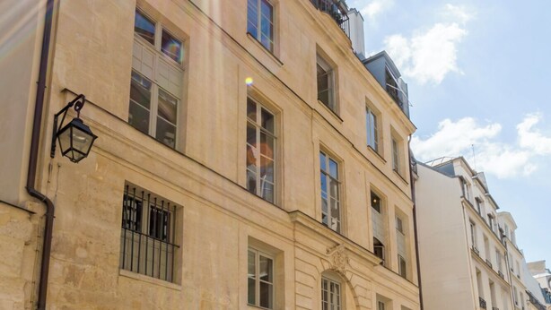 Un immeuble à plusieurs étages, de style architectural classique, qui se distingue par une entrée imposante avec une porte noire et des fenêtres ornées de barreaux en métal.