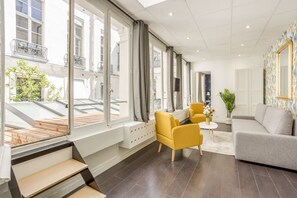 Un salon moderne avec un canapé gris, des fauteuils jaunes et un escalier en bois menant à un espace extérieur.