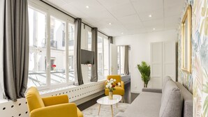 Une chambre d’hôtel moderne avec un canapé, deux fauteuils jaunes, une petite table ronde et une plante en pot.