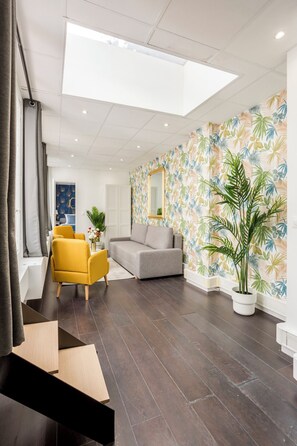A modern living room with a grey sofa, yellow armchair, and a large mirror on the wall. - Merveil - Family suite - Louvre - Victoires (Paris)