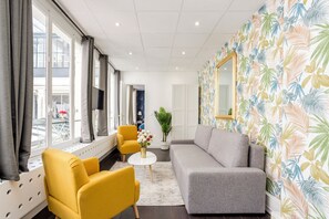 A modern hotel room with a sofa, two armchairs, a small table, and a large window with curtains. - Merveil - Family suite - Louvre - Victoires (Paris)